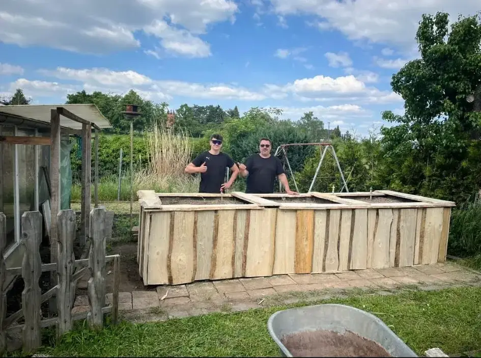 Zwei Männer hinter einem frisch gebauten Hochbeet aus Holz in einem Garten