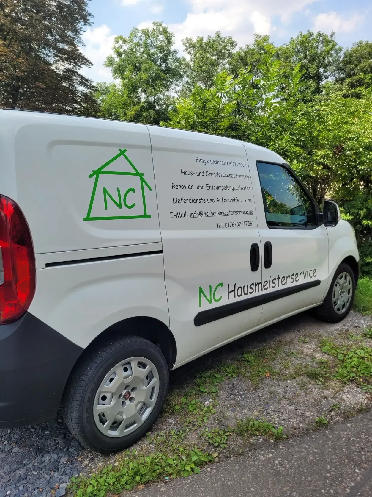 Weißer Transporter mit grünem NC-Hausmeisterservice-Logo auf einer Wiese